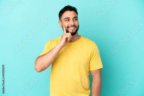 Young arab man isolated on blue background thinking an idea while looking up