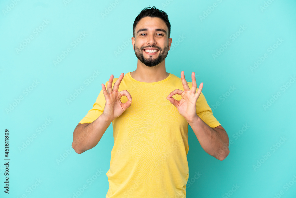 Young arab man isolated on blue background showing ok sign with two hands Young arab man isolated on blue background showing ok sign with two hands