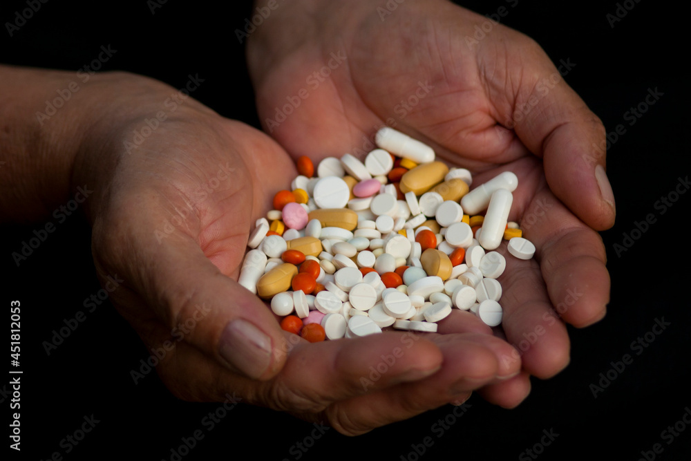 A handful of pills in male hands. A handful of various pills in male hands over black background A handful of pills in male hands. A handful of various pills in male hands over black background