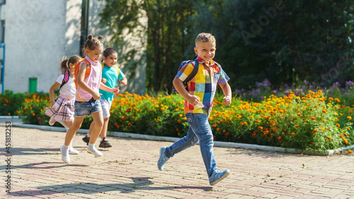 Fototapeta Naklejka Na Ścianę i Meble -  group of school children with backpacks run out of school, after the end of classes. Classmates, school friends. The beginning of holidays. The end of quarantine. Back to school.