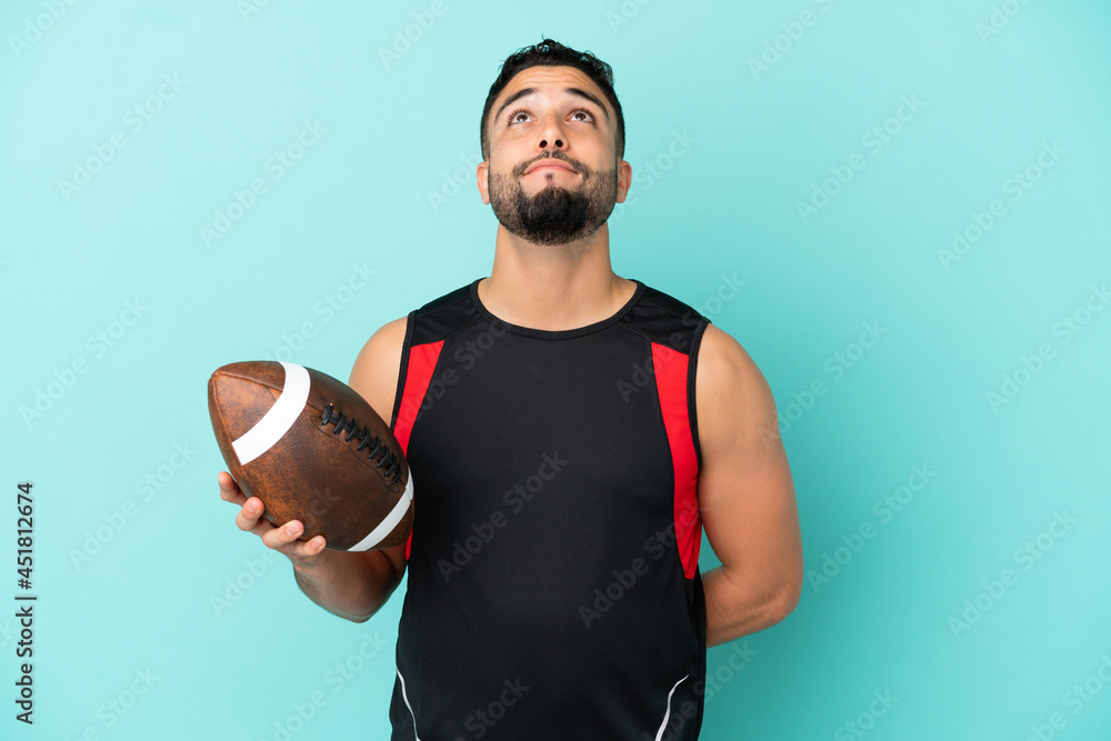 Young arab man playing rugby isolated on blue background and looking up