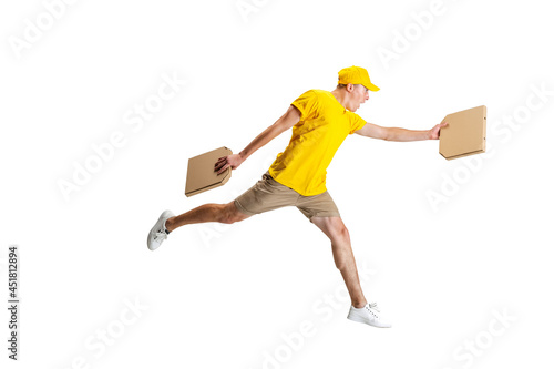 Young delivery man in yellow uniform running to deliver order isolated on white background. Concept of convenience, speed, comfort, safety, service. photo