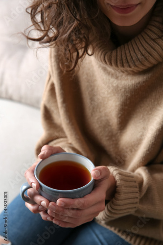 Woman with cup of hot tea indoors, closeup. Cozy home atmosphere