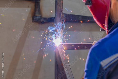 Working male welder with the help of a welding machine assembles the metal structure of the future staircase in a residential building. Sparks of hot metal are flying.