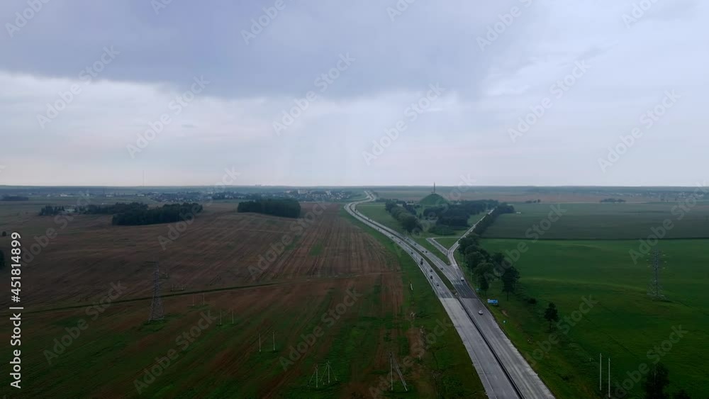 Aerial view of road and transport. People traveling by cars on a freeway. Memorial Mound of Glory in Belarus on background. Dramatic sky. Logistic and travel concept. Aerial view of road and transport. People traveling by cars on a freeway. Memorial Mound of Glory in Belarus on background. Dramatic sky. Logistic and travel concept.