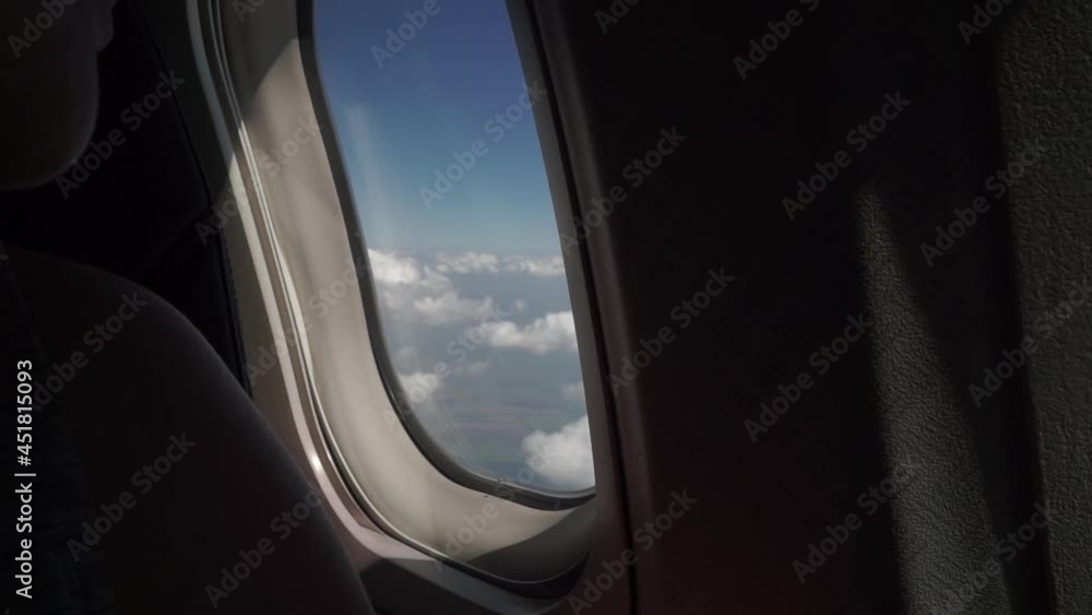 young girl sits, looks out window on an airplane, clouds, wing, blue sky, earth, fields. young girl sits, looks out window on an airplane, clouds, wing, blue sky, earth, fields.