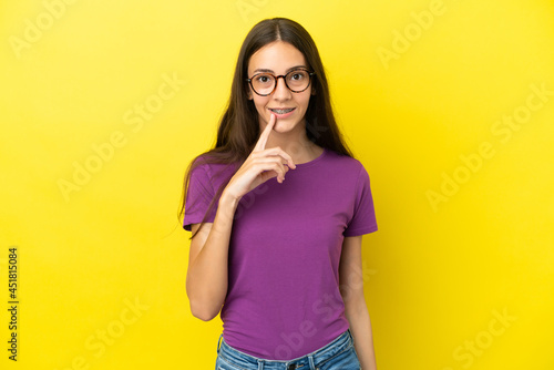 Young French woman isolated on yellow background showing a sign of silence gesture putting finger in mouth © luismolinero