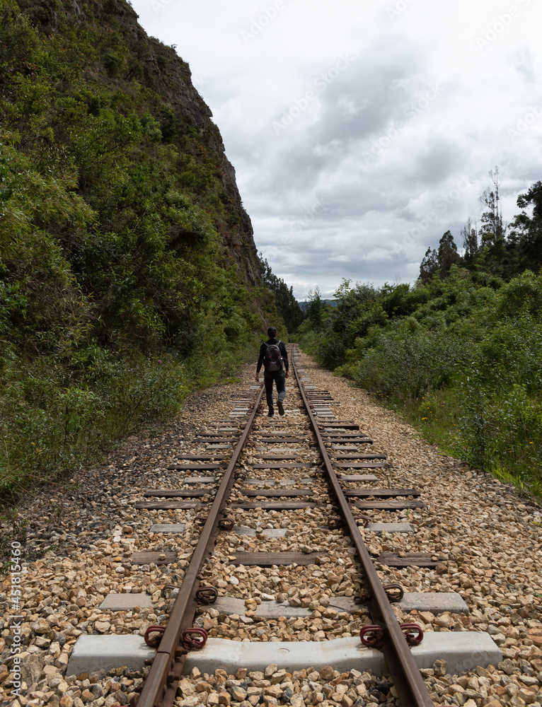Fototapeta premium un hombre vestido con ropa negra y mochila caminando en las vías del tren