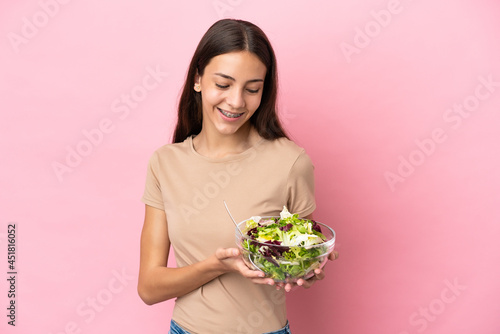 Young French girl isolated on pink background holding a bowl of salad with happy expression