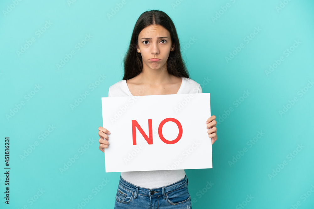 Young French woman isolated on blue background holding a placard with text NO with sad expression Young French woman isolated on blue background holding a placard with text NO with sad expression