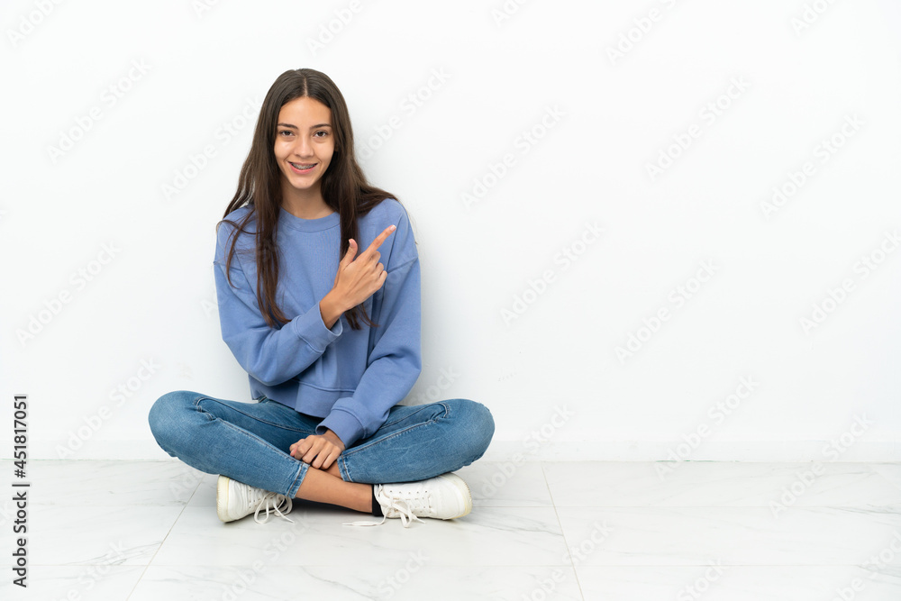 Young French girl sitting on the floor pointing to the side to present a product Young French girl sitting on the floor pointing to the side to present a product