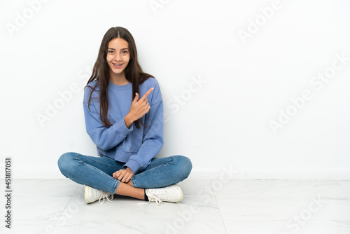 Young French girl sitting on the floor pointing to the side to present a product