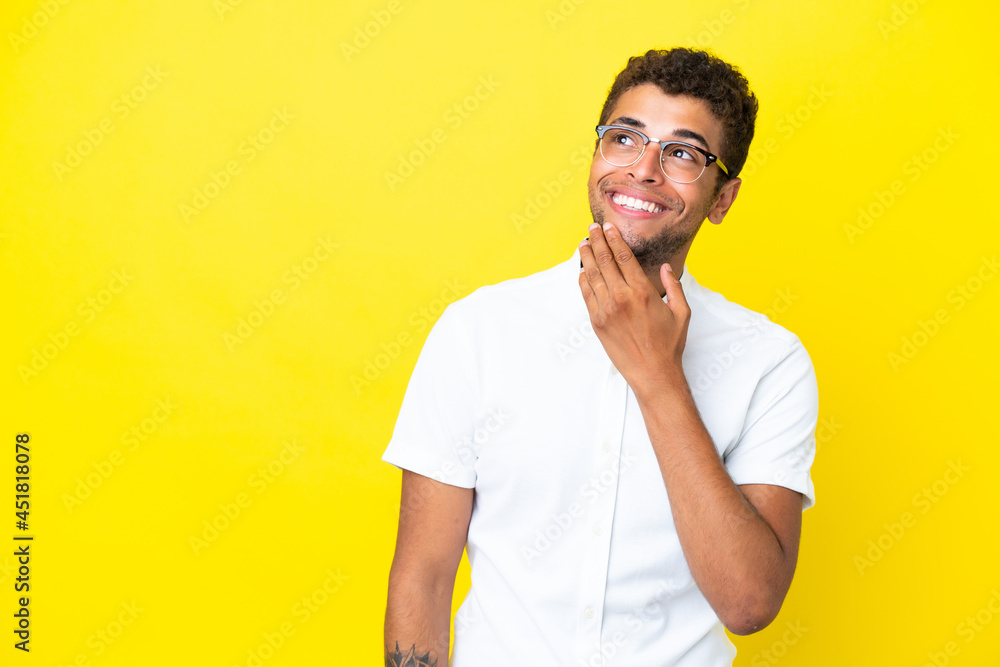 Young handsome Brazilian man isolated on yellow background looking up while smiling Young handsome Brazilian man isolated on yellow background looking up while smiling