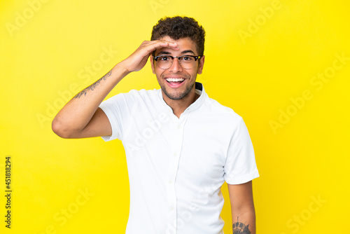 Young handsome Brazilian man isolated on yellow background looking far away with hand to look something