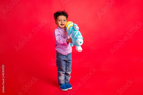 Full length body size view of attractive cheery guy holding water pump having fun isolated over bright red color background © deagreez