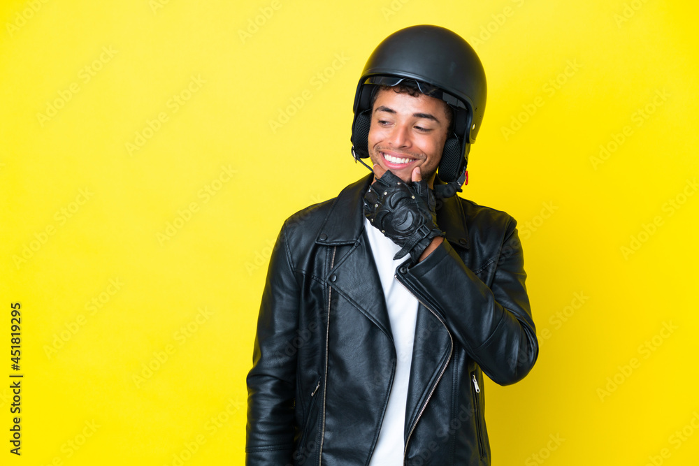 Young Brazilian man with a motorcycle helmet isolated on yellow background looking to the side and smiling Young Brazilian man with a motorcycle helmet isolated on yellow background looking to the side and smiling
