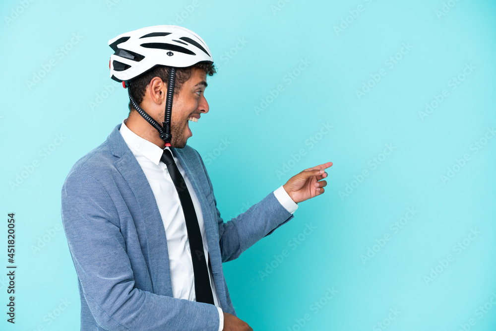 Young business Brazilian man with bike helmet isolated on blue background pointing finger to the side and presenting a product Young business Brazilian man with bike helmet isolated on blue background pointing finger to the side and presenting a product
