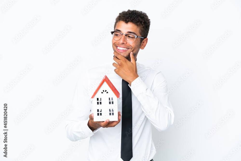 Young business Brazilian man holding a house toy isolated on white background looking to the side and smiling Young business Brazilian man holding a house toy isolated on white background looking to the side and smiling