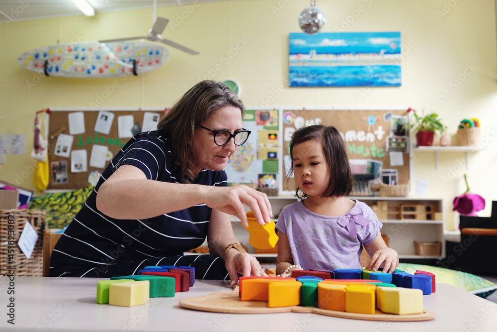 Multicultural teacher and child playing wooden blocks puzzles in