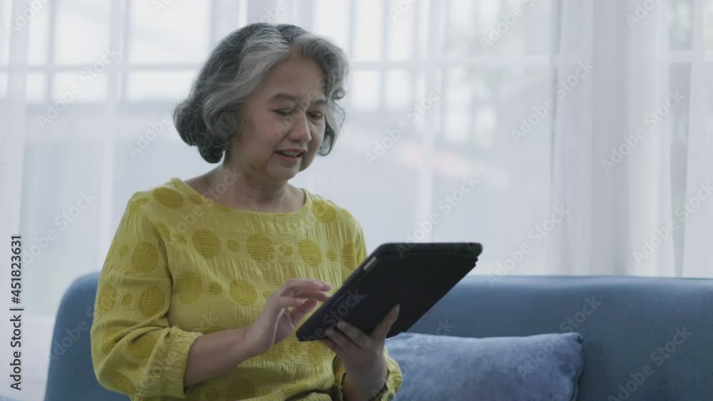 Asian elderly woman video calling and talking, smiling, happy family In living room. Stay at home. Telehealth consult doctor with tablet. Senior practice social play with tablet. Concept Telemedicine Asian elderly woman video calling and talking, smiling, happy family In living room. Stay at home. Telehealth consult doctor with tablet. Senior practice social play with tablet. Concept Telemedicine