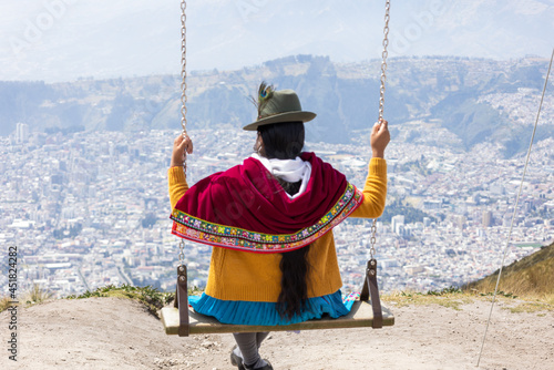 An indigenous Ecuadorian woman swinging on top of a tall mountain, looking down at the capital of Ecaudor, Quito.