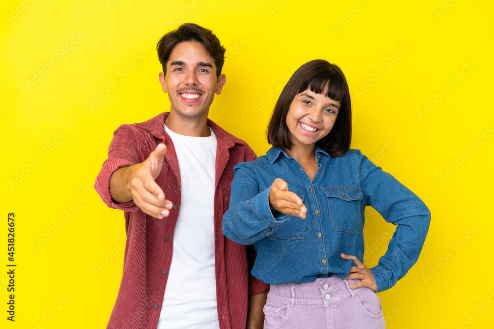 Young mixed race couple isolated on yellow background shaking hands for closing a good deal Young mixed race couple isolated on yellow background shaking hands for closing a good deal