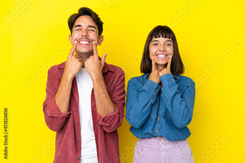Young mixed race couple isolated on yellow background smiling with a happy and pleasant expression