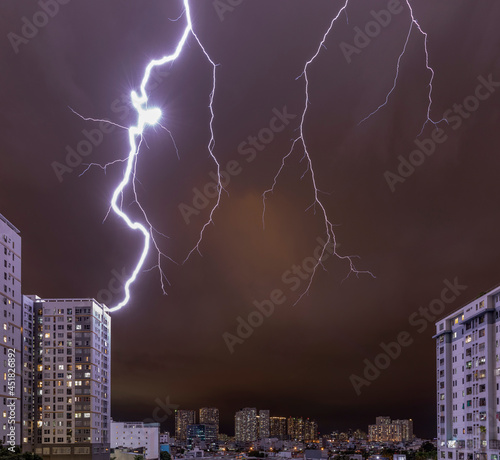lightning striking a high rise building at night with a red sky and illuminated urban setting during an electrical storm