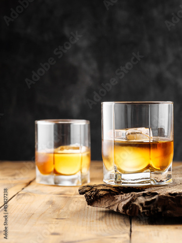 Two glasses with ice cube and whiskey on an old wooden table. Copy space.