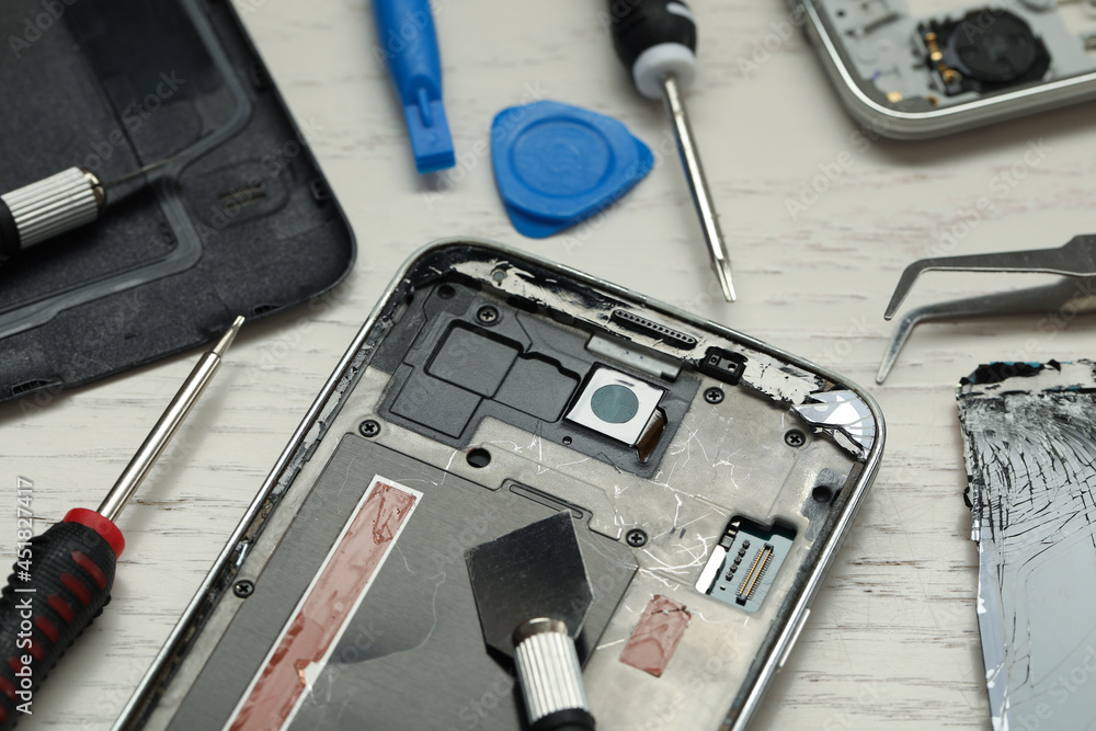 Parts of damaged smartphone and repair tools on light beige wooden table, closeup
