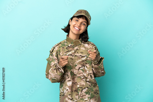 Military mixed race woman isolated on blue background points finger at you while smiling