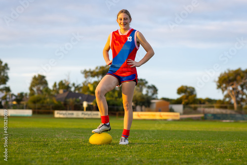 teenage girl in uniform standing on football oval with foot on ball