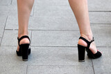 Female legs in black shoes on high heels, woman stands with her legs wide apart on a street. Ladies fashion and footwear, health of the feet, epilation concept