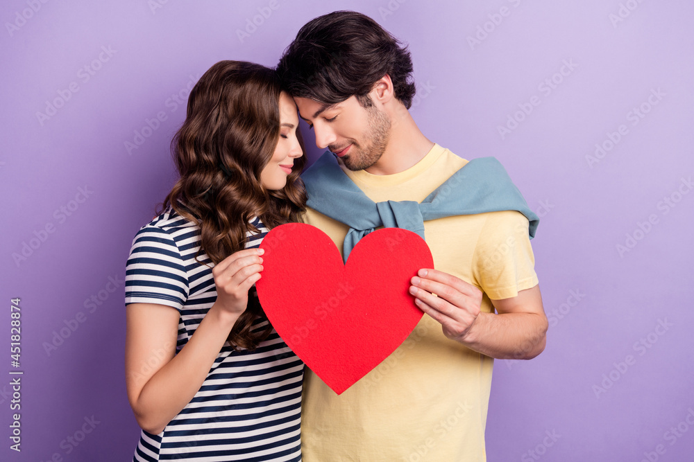 Photo of dreamy adorable couple wear casual clothes smiling holding large paper heart closed eyes isolated violet color background