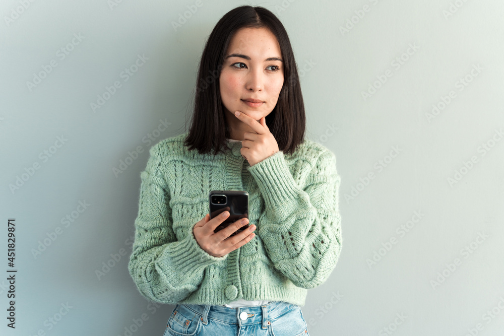 Portrait of romantic brunette woman using cellphone and pondering, reading good news message, enjoying mobile application. Indoor studio shot isolated on grey background Portrait of romantic brunette woman using cellphone and pondering, reading good news message, enjoying mobile application. Indoor studio shot isolated on grey background