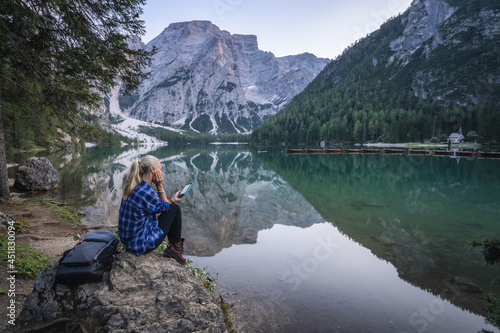 Woman reading e-book at Pragser Wildsee with reflected mountains on lake surface. Dolomites, Italy © Igor Tichonow