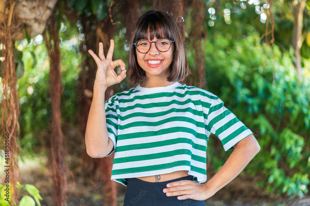 Young brunette woman at outdoors in a park showing ok sign with fingers