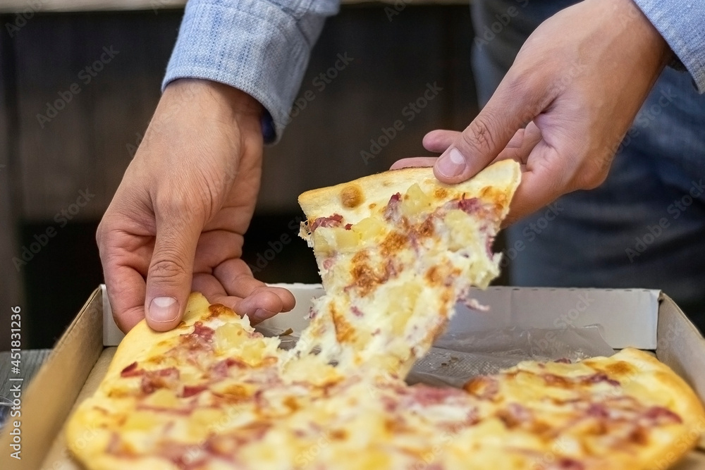 male hands take a slice of pizza from the box. hot slice of pizza with stretching cheese