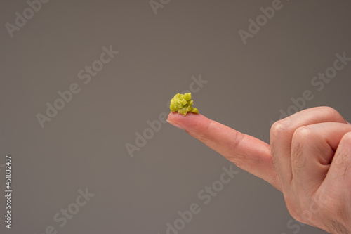 Fresh green Wasabi paste on the pointing fingers of a male hand. Close up studio shot isolated on brown background photo