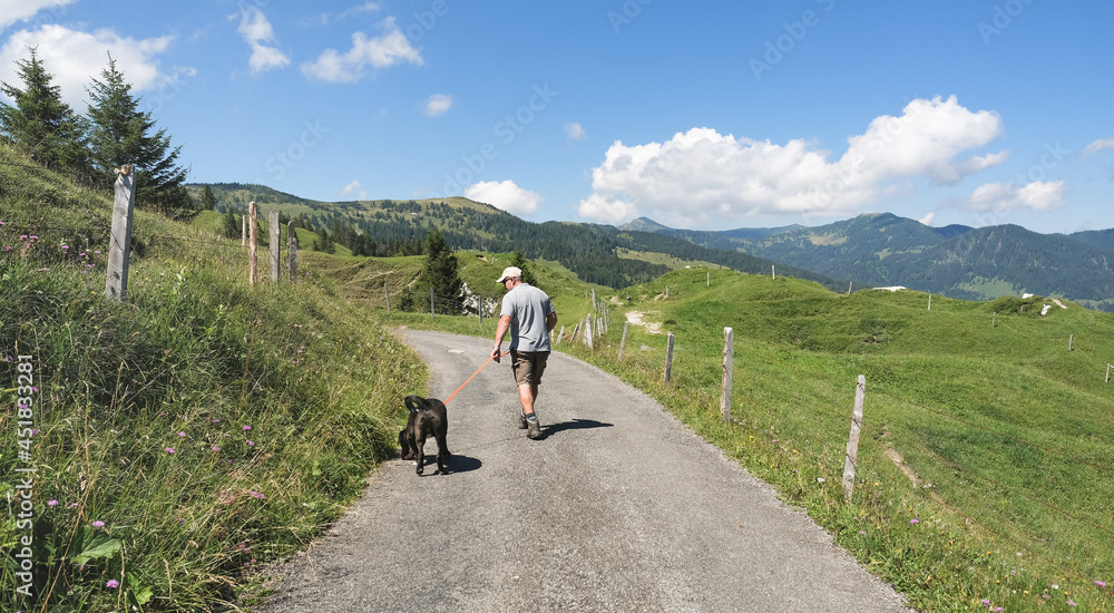 Active senior man walking outdoor with dog on a summer day - Mountain swiss panorama