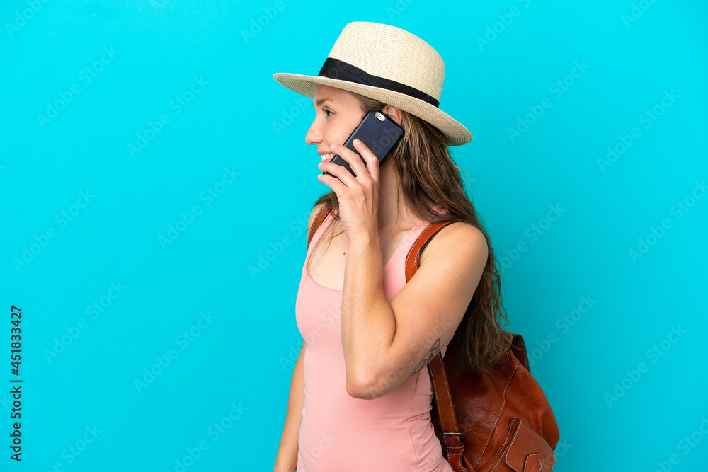 Young caucasian woman in summer holidays isolated on blue background keeping a conversation with the mobile phone with someone