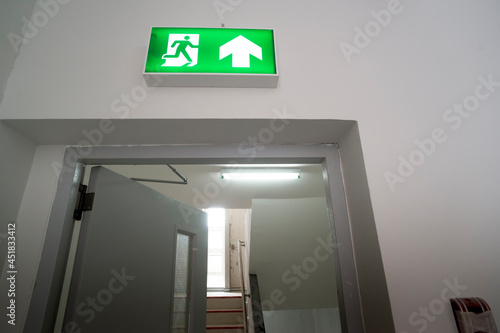 Sign   Emergency exit sign at path way indoor building public facility that emergency escape route is left.  fire  building  health or safety  require exit signs to be permanently lit