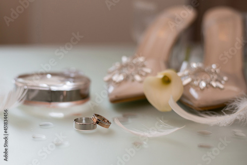 wedding rings next to the bride's shoes and feathers