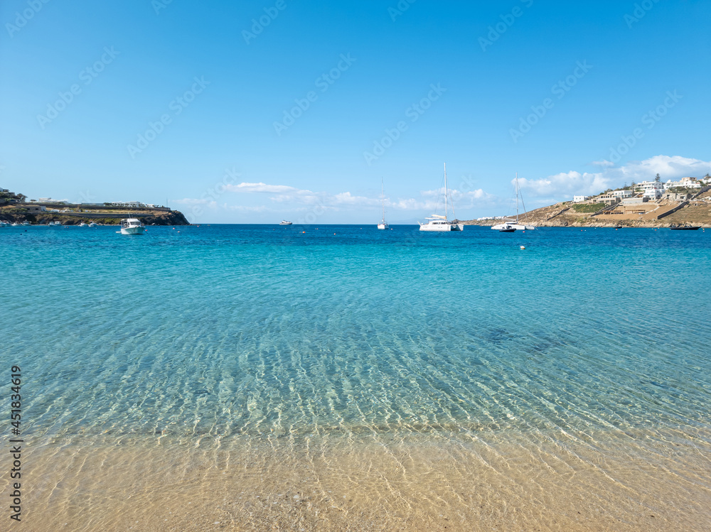 Ornos empty sandy beach, calm sea moored yachts background. Mykonos island, Cyclades Greece.