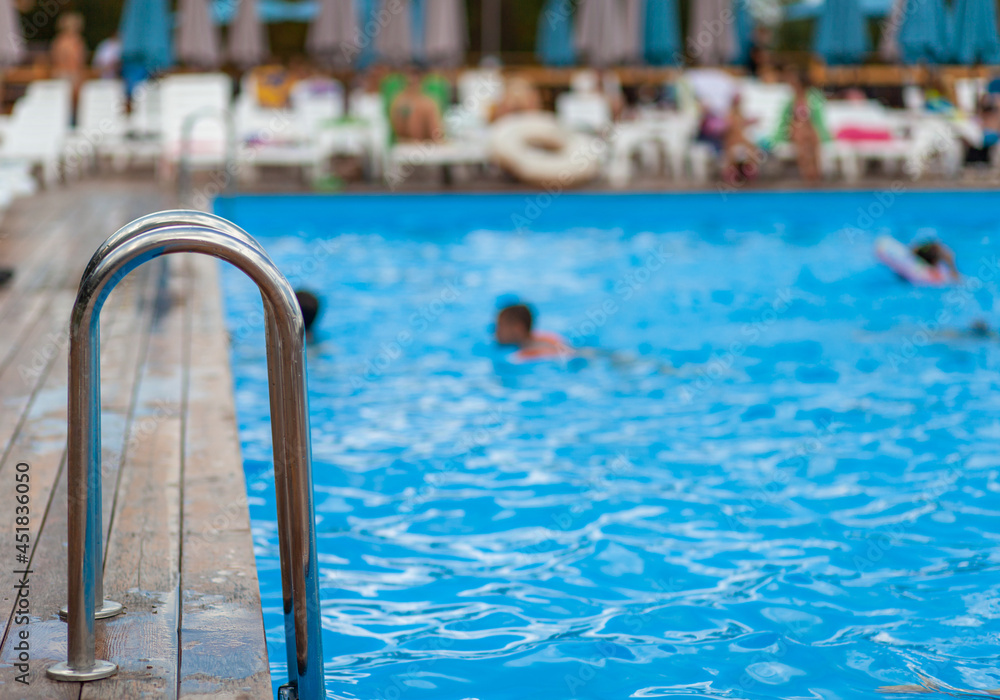 Ladder stainless handrails for descent into swimming pool. Swimming pool with handrail . Ladder of a swimming pool. People swim and relax in the pool