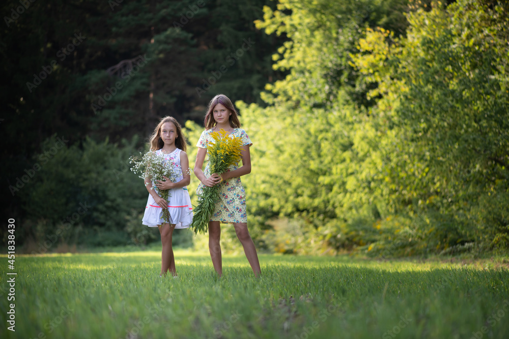 Two girls friends with bouquets of flowers are posing in the forest.