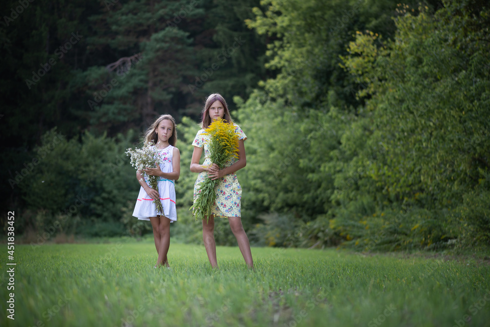 Two girls friends with bouquets of flowers are posing in the forest. Two girls friends with bouquets of flowers are posing in the forest.