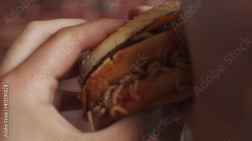 Man hand holds burger with maggots, bites and eats it, closeup. Man holds burger with maggots crawling on it and eats piece photo