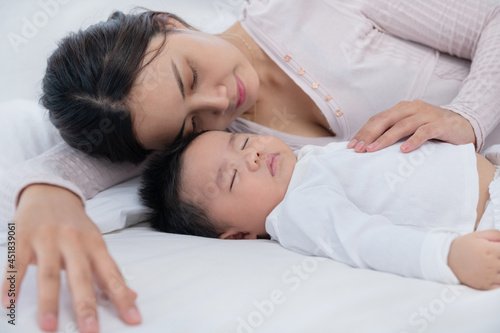 Loving mom carying of her newborn baby at home. Bright portrait of happy mum holding sleeping infant child on hands. Mother hugging her little 6 months old son. Family in the house. Lifestyle.