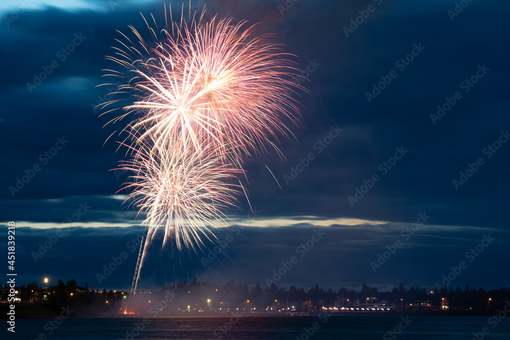Fireworks light up a cloudy night sky over a marina.